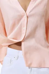 Camisa de corte holgado confeccionada en mezcla de lino y viscosa, de color rosado. Presenta cuello abierto, cierre frontal con botones, hombros caídos y mangas tres cuartos.