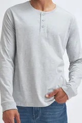 Remera de manga larga en color gris claro melange, confeccionada en tejido de punto suave. Presenta un cuello redondo con una pequeña abertura frontal cerrada por tres botones.