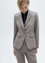 Blazer de corte recto en color beige, con cuello de solapa con muesca, cierre frontal de un botón y bolsillos laterales con solapa. Cuenta con forro interior y mangas largas con puños abotonados.