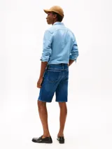 Bermuda de jean con diseño de cinco bolsillos, cierre de botón y cremallera, y corte recto. Presenta un acabado en tono azul medio con costuras reforzadas.