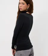 Blusa entallada de microfibra color blanco, con escote en V, mangas largas y detalle de frunces en los laterales. Presenta un lazo integrado en el cuello que permite anudarlo, aportando un toque sofisticado al diseño.