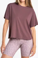 Remera deportiva color malva/ciruela, de manga corta y corte holgado, con cuello redondo y aberturas laterales en el ruedo.