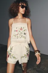 Top color crudo con tirantes finos y escote recto. Presenta bordado floral en el frente y detalle de encaje en el ruedo y escote.