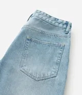 Pantalón de jean corte baggy, color celeste claro con efecto desgastado y estampado de lettering estilo grafiti en color blanco. Presenta cintura con trabillas, cierre frontal con botón y cremallera, y bolsillos laterales y traseros.
