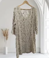 Vestido de tejido de punto calado color beige claro, con diseño floral y lentejuelas incrustadas. Tiene escote en V y mangas tres cuartos.