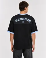 Remera de estilo deportivo con cuello en V y detalles en celeste. Presenta un estampado gráfico central con una escena de fútbol y la frase Sabremos Cumplir.