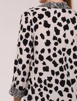 Camisa holgada de rayón con estampado animal print de manchas negras sobre fondo beige, cuello camisero y abotonadura frontal con detalles de estampa estilo cebra. Cuenta con mangas tres cuartos y ruedo curvo.