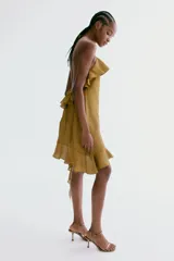 Vestido corto tostado de tiras finas halter, con escote decorado con volado amplio y bajo asimétrico con volado y tiras colgantes.