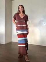 Vestido largo de tejido de punto de algodón, con diseño rayado en tonos marrón, celeste, blanco y rojo. Presenta escote en V con detalle de costura en contraste, mangas cortas, silueta holgada y aberturas laterales en el dobladillo.