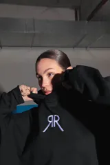 Buzo negro oversize de frisa con capucha amplia, bolsillo canguro, terminaciones de puño y ruedo con rib, y logo bordado en el centro delantero.