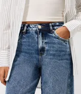 Pantalón de jean estilo wide leg con cintura media, cierre frontal con botón y cremallera, bolsillos funcionales y diseño de pierna amplia con recorte transversal.
