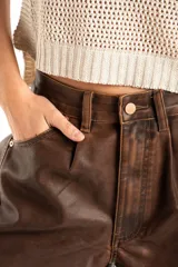 Bermuda de cuero vegano color marrón, con corte wide leg y tiro medio. Presenta diseño de cinco bolsillos y cierre frontal con botón metálico.