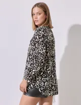 Blusa estampada en blanco y negro, marca Grand & Greene. Tiene cuello a la base, escote en V y abertura con botones. La manga es larga y amplia con detalle plisado.