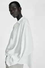 Camisa de cuello solapa y escote en pico, manga larga con puños y detalle de pliegues en el delantero. Presenta un diseño de bajo asimétrico.
