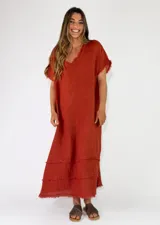 Vestido largo de lino color terracota, con escote en V y detalles de flecos en el cuello, mangas y en la parte inferior de la falda.
