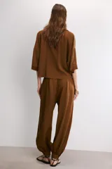 Pantalón de tiro alto en color beige, con diseño de pierna holgada y puños elásticos con cierre de botón en el bajo. Presenta cierre frontal con cremallera y doble botón en la cintura, además de bolsillos laterales.
