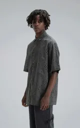 Camisa de manga corta con calce oversize, confeccionada en algodón con bordado tipo broderie y acabado con efecto desgastado. Presenta cuello clásico y cierre frontal con botones.