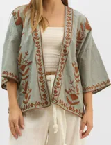 Cardigan tipo kimono de color verde con bordados florales en tono marrón a lo largo de los bordes frontales y en las mangas. Presenta un corte amplio y fluido con mangas tres cuartos.