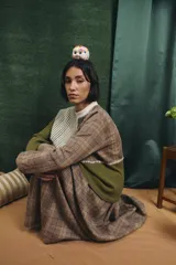 Buzo de manga larga con diseño patchwork que combina diferentes texturas y estampados, incluyendo tejido waffle verde oliva, tejido a rayas y cuadros en tonos grises y marrones, unidos con costuras visibles.