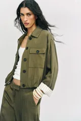 Chaqueta corta de color verde militar, con cuello solapa, bolsillos delanteros con solapa y cierre frontal de botones ocultos. Presenta mangas amplias con vuelta en los puños que muestran un forro a rayas.