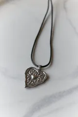 Collar con dije de acero quirúrgico hipoalergénico en forma de corazón con diseño texturizado y cordón encerado negro.