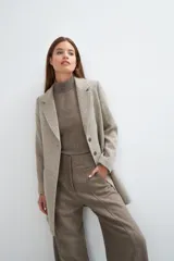 Saco corto entallado de lana fina, con cuello solapa, manga larga y cierre frontal con botones. Presenta un diseño clásico con textura de espiga en tonos tierra.