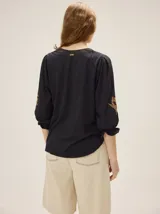 Remera de algodón de color negro con cuello en V y mangas tres cuartos abullonadas, con puños elásticos y detalles de bordado artesanal en las mangas.