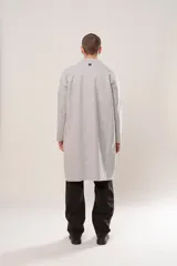 Sacón largo de corte recto y diseño abierto, confeccionado en tela simil paño color gris melange. Presenta mangas largas con terminaciones al corte, bolsillos ocultos y ruedo recto.