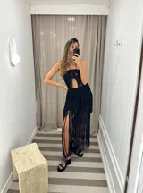 Falda larga de tejido de punto blanco, con cintura elástica y aberturas laterales. Presenta un largo fleco de hilo blanco en todo el ruedo.