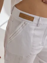 Pantalon de lino color blanco, de corte recto y tiro medio. Presenta costuras decorativas visibles, bolsillos laterales y cierre frontal con botón.