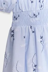 Vestido corto de color celeste con estampado floral, cuello redondo con volante y escote en pico. Presenta mangas cortas abullonadas con puños elásticos y cintura con nido de abeja elástico.