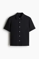 Camisa de manga corta confeccionada en tejido de punto con textura, cuello inglés, tapeta con botones y bajo recto con aberturas laterales.
