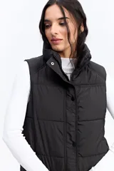 Chaleco puffer negro con cuello alto, cierre frontal y broches a presión. Diseño acolchado liviano con bolsillos laterales.