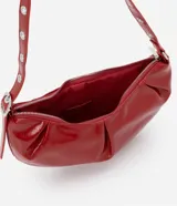 Cartera tipo shoulder bag de diseño media luna, confeccionada en poliuretano con acabado brillante. Presenta detalles frontales estilo gota, cierre superior por cremallera y correa de hombro ajustable con ojetes metálicos.