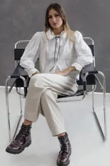 Camisa de voile de algodón en color blanco, con diseño romántico y corte holgado. Presenta detalles de encaje en color marfil en el frente y la espalda, cuello con blonda y pasa cinta, y mangas largas ligeramente fruncidas en los hombros con puños decorados.