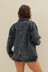 Campera de jean oversize en color negro con efecto acid wash, de mangas largas, cuello camisero, bolsillos frontales con solapa y cierre mediante botones metálicos.