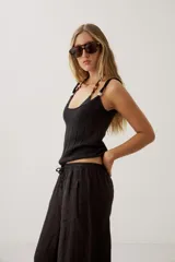 Top de punto negro con diseño acanalado vertical, escote redondo pronunciado y tirantes anchos con detalle de perlas o cuentas decorativas.