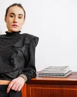 Camisa negra de lino con acabado brillante, cuello alto con volados, mangas largas abullonadas y detalles de volados frontales.