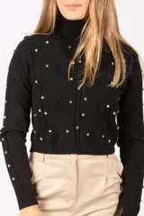 Sweater negro de cuello alto, con diseño de tejido trenzado y apliques de tachas metálicas circulares distribuidas por toda la prenda. Posee mangas largas con puños acanalados.