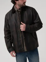 Chaqueta encerada de estilo clásico, color marrón oscuro, con cuello de cotelé y cierre frontal mediante broches a presión. Presenta un diseño de corte regular con bolsillos laterales integrados.