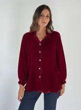 Camisa de terciopelo color borgoña, con cuello camisero, cierre frontal con botones y mangas largas abullonadas con puños elásticos.