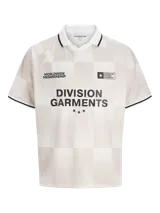 Camiseta de estilo fútbol con cuello polo, manga corta y corte holgado. Presenta un diseño de cuadros sutiles en tonos beige y blanco, con detalles de ribetes negros en cuello y mangas. Incluye estampados gráficos en el frente con texto y estrellas.