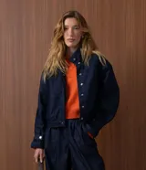 Campera bomber de denim azul oscuro, con cuello alto, cierre frontal con botones a presión ocultos, mangas largas con puños ajustables y diseño de largo corto.