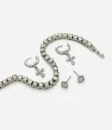 Kit de accesorios compuesto por dos pares de aros y una pulsera. Los aros incluyen un modelo de argolla con dije de cruz y un modelo de punto de luz. La pulsera es de estilo tenis con aplicaciones de strass. Todos los accesorios presentan un acabado metálico plateado.