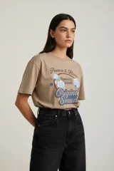 Remera de algodón de manga corta y cuello redondo, con diseño holgado y estampado gráfico frontal con motivos florales y tipografía vintage.