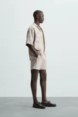 Bermuda de corte relajado color beige claro, confeccionada en lino. Presenta cintura elástica con cordón ajustable y bolsillos laterales y traseros.