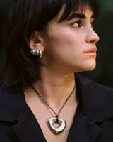 Collar con dije de forma irregular en tonos dorados y plateados, suspendido de un cordón doble de algodón negro.