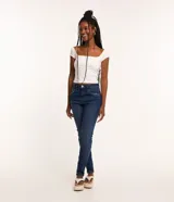 Pantalón de jean skinny azul oscuro con trabillas en la cintura, cierre tradicional por botón y cremallera, bolsillos delanteros y traseros deshilachados y costuras verticales.