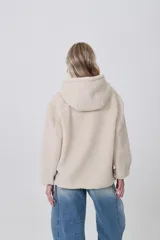 Campera de corderito con capucha, cierre frontal completo y bolsillos laterales. Presenta un diseño holgado de manga larga en color beige.