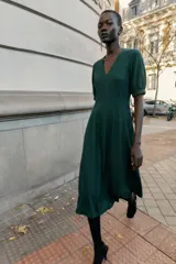 Vestido midi de color marrón chocolate, con escote en pico y mangas cortas abullonadas con puños elásticos. Presenta costuras verticales decorativas en el frente y cierre de cremallera oculta en la espalda.